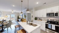 Located at 1025 Hirschfield Dr in Fayetteville, North Carolina, this single-floor residence offers a thoughtfully designed open-concept layout with modern finishes and a bright, welcoming ambiance throughout. The kitchen serves as the centerpiece of the home, featuring crisp white shaker cabinetry, a classic subway tile backsplash, stainless steel appliances, and a generous island with a built-in sink and bar seating — all illuminated by elegant brushed nickel pendant lights. Crown molding adds a refined architectural detail that carries through the main living areas. The living and dining spaces are bathed in natural light from large windows and a sliding glass door leading to an outdoor balcony, complemented by durable wood-look flooring underfoot. The bedrooms are comfortably sized, each equipped with ceiling fans and large windows that invite ample daylight. The primary suite includes a spacious walk-in closet outfitted with wire shelving and storage solutions, alongside a sleek en-suite bathroom featuring a glass-enclosed walk-in shower with floor-to-ceiling white tile. A second full bathroom offers a tub-shower combination with a white vanity. The home's clean, neutral palette and quality finishes create a cohesive and functional living environment.