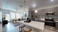 This stylish single-floor residence offers a thoughtfully designed open-concept layout that seamlessly connects the kitchen, dining, and living areas. The kitchen is a standout feature, equipped with stainless steel appliances including a French door refrigerator, electric range, built-in microwave, and dishwasher. Sleek grey flat-panel cabinetry, white quartz countertops, and a subway tile backsplash lend a clean, modern aesthetic, while a spacious kitchen island with seating provides both functionality and a natural gathering point. Pendant lighting and light wood-style flooring flow throughout the main living areas, creating a warm yet contemporary atmosphere. The living room is bright and welcoming, featuring large windows with sheer curtains that invite natural light, a ceiling fan, and access to an outdoor area. The bedroom is a comfortable retreat, carpeted for warmth, with a large window offering outdoor views, a ceiling fan, and ample space for a king-sized arrangement. The bathroom is finished with light wood-style flooring, a grey vanity with a white countertop, and a tub-shower combination accented by a bold patterned curtain. Recessed lighting and neutral tones throughout create a cohesive, modern ambiance.