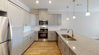 Located at 300 S Tulane Ave in Oak Ridge, Tennessee, this single-floor residence offers a thoughtfully designed layout with modern finishes throughout. The kitchen serves as a central highlight, showcasing granite countertops with subtle speckled detailing, a deep undermount stainless steel sink, and a suite of stainless steel appliances including a refrigerator, electric range, and over-the-range microwave. Gray shaker-style cabinetry lines the walls, complemented by a classic tile backsplash and recessed lighting, while elegant pendant lights hang above the kitchen island, adding warmth and visual interest. Light wood-tone flooring runs through the kitchen and connects seamlessly to adjacent areas. The bedroom features soft, neutral-toned carpet, warm beige walls, and a ceiling fan with integrated lighting, creating a comfortable and restful atmosphere. A paneled interior door and dedicated HVAC vent reflect practical, well-considered construction details. The bathroom is finished with wood-look vinyl plank flooring, a vanity with stone-topped counters, and clean white panel doors that echo the design language found throughout the unit. The overall aesthetic is contemporary and cohesive, with neutral tones and quality materials lending a polished, move-in-ready feel to this Oak Ridge residence.
