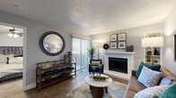This thoughtfully designed single-floor, one-bedroom, one-bathroom unit offers an efficient and comfortable layout across a compact yet functional footprint. The living room serves as the heart of the space, anchored by a white brick fireplace and complemented by wood-look flooring, a textured ceiling, and a sliding glass door that invites natural light while providing access to an outdoor area. The open flow from the entry hall — accented by a decorative round mirror and console table — connects seamlessly to the living and kitchen areas. The kitchen is well-equipped with white cabinetry, a blue-gray subway tile backsplash, stainless steel appliances including a range and over-the-range microwave, and a black refrigerator. Light wood-tone flooring and track lighting complete the kitchen's clean, modern aesthetic. The bedroom offers a cozy retreat with plush carpet, a ceiling fan, a natural-light window with blinds, and a dedicated closet. The bathroom features a full tub and shower combination with white tile surround and chrome fixtures. Throughout the unit, a neutral gray color palette and consistent design language create a cohesive and inviting atmosphere.
