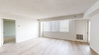 Located at 10301 Grosvenor Pl in Rockville, MD, this two-bedroom, two-bathroom residence offers a well-organized, single-floor layout designed for comfortable living. The open living room is bright and airy, featuring light hardwood flooring, a textured ceiling, and a large window dressed with vertical blinds that allows generous natural light to fill the space. The galley-style kitchen is thoughtfully appointed with granite countertops, warm wood cabinetry, stainless steel appliances including a refrigerator, electric range, built-in microwave, and dishwasher, all set over matching light hardwood floors. Both bathrooms are finished with white tile flooring and granite vanity tops with undermount sinks, maintaining a consistent design language throughout. The primary bedroom is a comfortable, well-sized retreat featuring plush carpeting, a large window with a balcony view of the surrounding landscape, and a closet. The second bedroom also features neutral carpet and ample wall space. A hallway connects the rooms, providing a functional flow through the residence. The clean, neutral palette throughout creates a bright, versatile atmosphere well-suited for a variety of living arrangements.