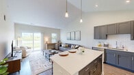 Located at 1700 64th Avenue in Kenosha, WI, this well-designed one-bedroom, one-bathroom home offers a thoughtful single-level layout with stylish finishes throughout. The heart of the home is the open-concept kitchen, dining, and living area, anchored by dramatic vaulted ceilings that create an airy, spacious feel. The kitchen is appointed with dark gray shaker cabinetry, white subway tile backsplash, stainless steel appliances, and a large white quartz island with seating — ideal for casual dining or entertaining. Pendant lighting above the island adds a modern touch. The living room flows seamlessly from the kitchen and is bathed in natural light from large sliding glass doors that open directly to a private patio, offering pleasant outdoor views. The bedroom is a comfortable retreat featuring plush carpet, natural light from multiple windows, and access to a well-organized walk-in closet with wire shelving. The bathroom is clean and modern, featuring a white vanity with quartz countertop, an illuminated mirror, and a glass-enclosed shower. A dedicated laundry room with full-size washer and dryer adds everyday convenience. Wood-look flooring runs throughout the main living areas, tying the space together with a warm, cohesive aesthetic.
