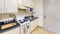 Located at 123 Prospect St in Ithaca, NY, this single-floor unit offers a thoughtfully organized layout designed for comfortable everyday living. The living area is a standout feature, bathed in natural light streaming through a wide bank of windows fitted with horizontal blinds. The space accommodates a full sofa, armchairs, and a coffee table, creating a welcoming and functional environment. A dedicated corner seating nook with additional armchairs and a window view adds extra versatility to the living space.

The kitchen is compact yet fully equipped, featuring a coil-burner range, an overhead exhaust hood, a microwave, dark countertops, and cream-colored cabinetry that maximizes storage. A double-basin sink and tile-style flooring complete the practical setup.

The bedroom is quietly tucked away, offering a serene retreat with clean white walls, wall-mounted lighting, a single bed, and a dedicated study area with a wooden desk, chair, and bookshelf — ideal for focused work or study.

The bathroom is accessible via a rich dark wood door and features tile-style flooring, neutral walls, and a bathtub-shower combination enclosed with sliding frosted glass doors, providing both function and privacy throughout the unit.