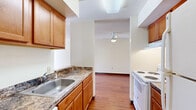 Located at 46558 Valley Ct in Lexington Park, Maryland, this two-bedroom, one-bathroom home offers a well-organized single-floor layout with consistent hardwood flooring throughout. The living room serves as the heart of the home, highlighted by a classic black-surround fireplace, a front entry door, and large windows that allow generous natural light to fill the space. A ceiling fan adds to the room's comfort and functionality.

The galley-style kitchen is efficiently designed, featuring warm wood cabinetry, granite-style countertops, a stainless steel sink, and white appliances including a range and refrigerator. The kitchen connects seamlessly to the living area, enhancing the flow of the home. A utility area with an electrical panel is also accessible from the kitchen corridor.

Both bedrooms are bright and well-proportioned, with hardwood floors and large windows — including a sliding glass door with vertical blinds in the primary bedroom that invites outdoor views and natural light. The shared full bathroom includes a wood vanity with a white countertop, mirror, and hardwood flooring that continues from the rest of the home. A hallway and utility room round out the functional layout of this clean, move-in ready residence.