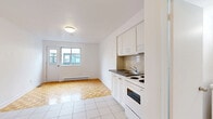 Located at 1240-1250 Rue du Fort in the heart of Montréal, this studio offers a well-organized, single-floor layout designed to maximize functionality within a compact footprint. The open living area features warm parquet flooring in a classic block pattern, lending a timeless character to the space. A large sliding window allows natural light to fill the room and offers a view of the surrounding neighbourhood, while a baseboard heating system ensures comfort throughout the seasons. The kitchen is efficiently arranged along one wall, outfitted with white cabinetry — both upper and lower — a dark countertop, a double-coil electric range with oven, and a stainless steel sink. White floor tiles extend through the kitchen and entryway, creating a clean visual transition from the living area. A dedicated closet near the entrance provides convenient built-in storage. The bathroom is finished in white tile, featuring a full-size soaking tub with shower, a toilet, and a vanity with storage. The overall palette of the studio is bright and neutral throughout, with white walls and ceilings contributing to an open, airy ambiance. This studio is situated in a vibrant Montréal neighbourhood, offering easy access to urban amenities.