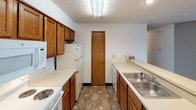 This single-floor unit features three bedrooms, two bathrooms, and a practical, well-organized layout. The galley-style kitchen is outfitted with warm oak cabinetry, white appliances including a electric range, microwave, refrigerator, and dishwasher, and durable tile-style flooring. A peninsula counter connects the kitchen to the open living area, offering a convenient pass-through between the two spaces. The living room is generously sized, finished with wall-to-wall carpet, baseboard heating, a wall-mounted air conditioning unit, and a sliding glass door that opens to a private balcony with outdoor views. Each of the three bedrooms features neutral carpet, textured ceilings, baseboard heating, and windows with blinds that allow natural light while maintaining privacy. One bedroom also includes a wall-mounted air conditioning unit. The bathrooms are cleanly appointed, with one featuring a full soaking tub and shower combination, a single-sink vanity with oak cabinetry, and a framed mirror. Throughout the unit, the design is straightforward and functional, with a neutral color palette, textured ceilings, and consistent warm-toned wood accents that provide a cohesive, comfortable feel.