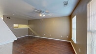 This two-story home offers a well-organized layout across two floors, comprising two bedrooms, three bathrooms, and four closets. The main level features a combined dining room, kitchen, and living room that flows naturally together. The living room is finished with rich, dark hardwood-style flooring, warm neutral-toned walls, a ceiling fan with light fixture, and windows that allow natural light to fill the space. A staircase with white-trimmed railing connects the entry area to the upper level. The kitchen is laid out in a galley style, featuring white cabinetry with wood-tone trim, white appliances including a coil-top electric range, dishwasher, and refrigerator, along with ample upper and lower cabinet storage and a double sink. The bathrooms include a vanity with countertop and a tub-shower combination. The bedrooms are located on the upper floor and are carpeted for comfort, each equipped with a ceiling fan, neutral painted walls, and windows providing natural light. The primary bedroom is notably spacious with two windows. Additional storage is provided throughout via four closets. The overall aesthetic is consistent and practical, with warm earth-tone walls, white trim, and a mix of hard and soft flooring surfaces throughout.