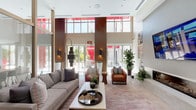Located at 1622 S Magnolia Ave in Monrovia, California, this contemporary single-floor amenity space is designed to impress with its sophisticated architecture and thoughtfully curated interiors. The centerpiece is a soaring double-height lounge area flooded with natural light from expansive floor-to-ceiling windows and clerestory glazing. Bold red architectural accents contrast with warm wood-paneled columns and crisp white walls, creating a dynamic and inviting atmosphere. The lounge is furnished with plush sofas, leather accent chairs, a wall-mounted fireplace, and curated artwork, all anchored by a large area rug.

A glass-partitioned room adjacent to the lounge offers a more intimate gathering space, visible through wood-framed panes and illuminated by pendant lighting. The full-scale demonstration kitchen features sleek gray cabinetry, quartz countertops, stainless steel appliances including multiple ovens and a gas cooktop, and textured stone wall accents with integrated shelving and a mounted television.

A game room with herringbone hardwood flooring houses a full-sized billiards table, while a separate casual dining nook showcases sculptural live-edge high-top tables paired with leather bar chairs and vibrant contemporary wall art. Together, these areas offer a well-rounded, upscale communal environment.