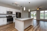 This single-story unit in Macon, Georgia offers a well-designed, open-concept layout that balances functionality with modern finishes throughout. Warm hardwood-style flooring extends across the main living areas, complemented by ceiling fans that contribute to a comfortable, airy atmosphere.

The kitchen serves as a central feature, equipped with stainless steel appliances including a range, over-the-range microwave, and refrigerator. White shaker-style cabinetry pairs with granite countertops and a classic subway tile backsplash, creating a clean, contemporary aesthetic. A kitchen island with pendant lighting provides additional workspace and a natural gathering point. A dedicated walk-in pantry offers generous storage directly off the kitchen. A built-in desk nook adds a practical workspace to the common area.

The living room is spacious and bright, featuring a sliding glass door that opens to a private balcony with outdoor views, inviting natural light deep into the space. Bedrooms feature plush carpeting and large windows that frame outdoor greenery, enhancing the sense of comfort and calm.

The bathroom includes a tub-shower combination with built-in shelving, white cabinetry with granite countertops, and coordinating hardwood-style flooring, maintaining the consistent, polished finish found throughout the unit.