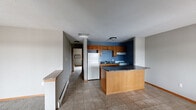 Located in Marion, Iowa, this single-floor unit offers a functional and straightforward layout designed for comfortable everyday living. The kitchen is a standout feature, showcasing warm honey-toned oak cabinetry, dark granite-style countertops, and a bold navy accent wall that adds a pop of color. A large peninsula provides additional prep space and casual seating, while tile flooring and included appliances — including a refrigerator and range — complete the space. The kitchen flows openly toward the main living and dining areas, where large windows and sliding glass door access to a balcony bring in generous natural light and outdoor views of surrounding trees and neighboring rooftops. Bedrooms are carpeted for comfort, finished with neutral gray walls, warm wood-trimmed doors, and ceiling fans for climate control. Baseboard heating runs throughout the unit, and select rooms feature wall-mounted air conditioning units. The layout, as seen in the dollhouse view, is well-organized with clearly defined living, kitchen, and sleeping zones connected by a central hallway. Warm wood baseboards and trim provide a consistent, cohesive aesthetic throughout this practical Marion residence.