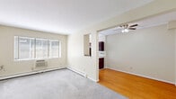 This two-bedroom, one-bathroom residence at 2086 Stanley St in New Britain, CT offers a practical and well-organized single-floor layout. The living room is a comfortable, carpeted space bathed in natural light from a large window with blinds, and features baseboard heating and a wall-mounted AC unit. A pass-through opening connects the living area to the adjoining dining and kitchen zone, which is finished with warm hardwood-style flooring and a ceiling fan overhead. The kitchen is galley-style, equipped with rich dark cabinetry, granite-look countertops, a stainless steel refrigerator, and tiled flooring — providing ample storage and counter space. Both bedrooms are carpeted in neutral tones with cream-colored walls, windows with natural light, and baseboard heating. The primary bedroom includes a closet with built-in shelving, while the second bedroom also features closet space. Two hallways connect the rooms efficiently throughout the unit. The bathroom is finished with light tile flooring, a dark vanity with a mirror cabinet, and a shower-tub combination enclosed by sliding glass doors. Overall, the space presents a clean, functional aesthetic well-suited for comfortable everyday living.