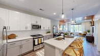 Located at 554 Lancaster Ave in Malvern, PA, this well-appointed 1-bedroom, 2-bathroom residence offers a thoughtfully designed single-floor layout with an open, contemporary feel. The kitchen is a standout feature, showcasing white shaker upper cabinets, grey lower cabinetry, a classic subway tile backsplash, quartz countertops, stainless steel appliances including a gas range, and a central island with bar seating and globe pendant lighting — all flowing seamlessly into the dining and living areas. The living room is characterized by warm, boldly accented walls, wood-look flooring, large windows that invite natural light, a ceiling fan, and direct access to a private patio with outdoor views of the landscaped surroundings. The bedroom is comfortably sized and served by two closets. The two bathrooms are finished with neutral tones, quartz vanity surfaces, black hardware accents, and hardwood-style flooring; one features a walk-in glass-enclosed shower. Additional practical spaces include a dedicated laundry area and a utility room. The overall design balances modern finishes with a warm color palette, creating a cohesive and inviting living environment.