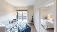 This one-bedroom, one-bathroom unit at Indigo is thoughtfully designed with a modern aesthetic and functional layout across a single floor. The open-concept living area features warm wood-look flooring, neutral walls, and large sliding glass doors that lead to a private balcony, filling the space with natural light and providing outdoor views.

The kitchen is a standout feature, equipped with stainless steel appliances including a refrigerator, range, and microwave. White shaker-style cabinetry extends to the ceiling, complemented by a subway tile backsplash, light quartz countertops, and a undermount sink. A kitchen island provides additional prep and seating space, making the area well-suited for both cooking and casual dining. Track lighting overhead ensures ample illumination throughout.

The bedroom is a calm, well-proportioned retreat with soft neutral tones, a large window allowing natural light, and sufficient space for full-sized furniture. A walk-in closet is accessible nearby for added storage.

The bathroom features wood-look flooring consistent with the rest of the unit, white cabinetry with modern hardware, a tub-shower combination with white tile surround, and clean, minimalist finishes that maintain the unit's cohesive contemporary style.