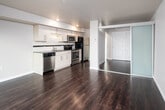 This well-appointed single-floor unit offers a thoughtful layout that balances open living with functional private spaces. Rich, dark hardwood flooring runs continuously throughout, providing a cohesive and elegant foundation for the entire space.

The kitchen is a standout feature, outfitted with modern white cabinetry, dark granite-style countertops, a subway tile backsplash, and a full suite of stainless steel appliances including a dishwasher, range, microwave, and refrigerator. Recessed lighting above ensures the space is well-lit and practical.

A central hallway connects the rooms efficiently, with clean white doors, bright trim, and built-in closet storage along the way. The hallway leads to a generously sized bedroom featuring a double sliding closet with paneled doors and neutral warm-toned walls, creating a calm and restful environment.

The living area is notably bright and open, anchored by a large floor-to-ceiling sliding glass window and door that frames expansive views of the surrounding neighborhood and cityscape, flooding the space with natural light.

The bathroom is cleanly finished with a wide vanity topped with a dark countertop, an undermount sink, a full tub-shower combination, and a large mirror that enhances the sense of space. The overall design is contemporary, cohesive, and move-in ready.