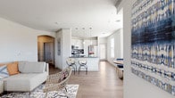 This single-floor residence is designed around an open-concept floor plan that seamlessly connects the living, dining, and kitchen areas into one cohesive, well-lit space. Light wood-tone flooring runs throughout the main living areas, complemented by crisp white walls and crown molding that lend a clean, polished character to the interior.

The kitchen is a standout feature, outfitted with white shaker-style cabinetry, dark granite countertops, a textured tile backsplash, and a full suite of stainless steel appliances including a refrigerator, range, microwave, and dishwasher. A peninsula with bar seating serves as both a functional workspace and a casual gathering spot. Pendant lights hang overhead, adding focused illumination and a modern touch.

Adjacent to the kitchen, a dining nook is framed by a trio of windows that invite natural light and offer views of the surrounding area. The living room provides generous space for seating, enhanced by crown molding and an arched passageway that adds architectural interest.

The bedroom features plush carpeting, a ceiling fan, and a window that brings in natural light. The bathroom is finished with white cabinetry, granite counters, wood-look flooring, and a tiled tub-shower combination.
