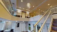 Located at 1455 Washington Blvd in Stamford, Connecticut, this two-story commercial space makes a strong first impression with a dramatic double-height entrance lobby. The centerpiece of the ground floor is a cascading crystal chandelier that hangs from the soaring ceiling, drawing the eye upward and adding a refined, upscale character to the entryway. Large glass-paneled entry doors allow natural light to pour into the lobby, creating a bright and welcoming atmosphere.

The ground floor features warm-toned tile flooring throughout, white wainscoting with classic panel molding, and a seating area near the entrance with modern leather chairs — ideal for receiving guests. An elevator provides convenient vertical access alongside a broad staircase with wood and metal railings that connect to the upper level.

The second floor opens to a spacious landing with the same tile flooring, recessed lighting, and a continuous railing overlooking the lobby below. This level includes a reception or service counter area along one wall, additional doorways leading to private spaces, and wall art that adds a contemporary touch. The two-tone wall treatment — dark lower panels contrasting with lighter upper walls — carries through both floors, lending a cohesive and professional aesthetic throughout the building.