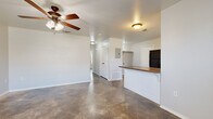 This single-story residence offers a functional and straightforward layout designed for comfortable everyday living. The open-concept living area flows directly into the kitchen, creating a connected and sociable space. The living room features a ceiling fan with integrated lighting and durable tile flooring that extends throughout the home, providing a cohesive and easy-to-maintain surface underfoot.

The kitchen is well-equipped with white cabinetry, black appliances including a refrigerator, range, microwave, and dishwasher, and a peninsula with a warm-toned countertop that doubles as a breakfast bar. A window above the sink allows natural light into the cooking area, and a door provides direct exterior access.

The bedrooms are generously proportioned, each outfitted with ceiling fans and tile flooring. One bedroom includes a closet with a hanging rod, while another benefits from a window fitted with blinds for natural light and privacy. The hallway connecting the rooms features additional closet and utility access, including an electrical panel.

The bathroom includes a clean, all-white stand-up shower with bronze hardware accents. Throughout the home, neutral wall tones, white trim, and consistent flooring create a calm, uniform aesthetic. The overall layout, as seen in the dollhouse view, is compact yet efficiently organized for single-floor living.
