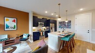 Located at 100 Fulton St SE in Atlanta's Grant Park neighborhood, this single-floor residence blends contemporary design with vibrant personality. The open-concept layout connects the kitchen, dining, and living areas into one cohesive, light-filled space. The kitchen is a standout feature, outfitted with bold navy cabinetry accented by gold hardware, stainless steel appliances, and a spacious white quartz island with bar seating — ideal for both cooking and casual dining. Brass globe pendant lights overhead add a warm, modern touch. The living area is anchored by a large window and glass door that draw in natural light, creating an airy and welcoming atmosphere. Warm-toned accent walls add depth and character throughout the main living space. Hardwood-style flooring flows through the common areas, while plush carpet adds comfort to the bedrooms. The primary bedroom features a ceiling fan, natural light through blinded windows, and direct access to a well-appointed bathroom with matching navy cabinetry and a walk-in closet. A second bedroom offers a cozy retreat with warm yellow walls and ample space. The overall design balances bold color choices with clean, modern lines for a dynamic yet functional living environment.