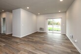 This single-story residence in Waukee, Iowa offers a thoughtfully designed layout that maximizes functionality and comfort. The open-concept kitchen and living area forms the heart of the home, finished with light-toned luxury vinyl plank flooring that runs throughout the main living spaces. The kitchen is equipped with stainless steel appliances — including a refrigerator, range, microwave, and dishwasher — complemented by warm-toned wood cabinetry and recessed lighting overhead. The living area is bright and airy, featuring a sliding glass door that invites natural light and provides views of the surrounding greenery outside. Neutral gray walls and clean white trim maintain a consistent, modern aesthetic throughout. The bedroom is carpeted for added comfort, fitted with a ceiling fan, and benefits from a large window that brings in natural light. It includes access to a walk-in closet outfitted with wire shelving for organized storage. The full bathroom features a tub/shower combination, a vanity with a light countertop, and wood-look flooring. Additional highlights include a dedicated laundry area, a utility room, a hallway connecting the private spaces, and two closets for ample storage. The overall ambiance is clean, contemporary, and move-in ready.