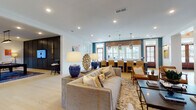 Located at 5360 Cherokee St in Acworth, GA, this thoughtfully designed single-floor communal space blends contemporary style with warm, inviting elements across several distinct yet connected areas. Light hardwood flooring runs throughout, unifying the open layout and complementing the bright white walls and crisp crown molding.

The main lounge area centers around a generously sized sectional sofa accented with layered throw pillows, a patterned area rug, and a rustic console table adorned with bold blue ceramic lamps and sculptural gold décor. Built-in dark navy shelving units display curated accessories and artwork, adding depth and contrast to the space. Recessed lighting illuminates the area throughout.

An adjacent game room features a pool table set against a dramatic dark-paneled wall with integrated shelving and a wall-mounted TV, creating a dedicated entertainment zone. A long white-countertop bar with warm wood accents and woven rattan barstools seats multiple guests beneath striking pendant lights, with large windows providing ample natural light and outdoor views.

A charming banquette nook offers an intimate retreat, featuring a tufted caramel leather bench, decorative bird-print wallpaper, a wood accent wall, and an artistic geometric chandelier — ideal for casual gatherings. The overall ambiance is polished yet approachable, balancing modern design with comfortable functionality.
