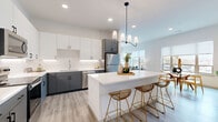 This contemporary 2-bedroom, 2-bathroom residence is thoughtfully designed across a single floor, offering an efficient and stylish open-concept layout. Light wood-tone flooring runs throughout, complementing the clean white walls and modern finishes that define the space.

The kitchen is a standout feature, showcasing two-tone cabinetry with crisp white upper cabinets and charcoal-gray lower cabinets, white quartz countertops, a subway tile backsplash, and a full suite of stainless steel appliances. A central island with seating provides both additional prep space and a casual dining option, illuminated by an elegant pendant chandelier.

The open living and dining areas are filled with natural light from large windows that frame views of the surrounding cityscape. The dining nook, positioned beside a wide window, offers an airy setting, while the living room benefits from an expansive multi-panel window arrangement.

Both bedrooms are comfortably sized, with the primary bedroom offering generous proportions and a dedicated closet. Each room features large windows with roller shades, continuing the bright and airy aesthetic. The two bathrooms are finished with the same charcoal cabinetry, white countertops, and wood-look flooring — one featuring a soaking tub and the other a dual-sink vanity with a large mirror.