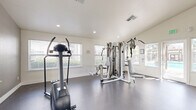 Located at 1501 Cobble Creek Circle in Rocklin, California, this fitness center offers a well-equipped workout facility designed to support a variety of exercise routines. The space features vaulted ceilings that lend an open, airy feel, while large windows fitted with blinds allow ample natural light to fill the room throughout the day. The durable rubber-coated flooring provides a safe and functional surface suited for both cardio and strength training activities.

The facility is outfitted with a comprehensive range of equipment, including a multi-station cable and weight machine, a treadmill, an elliptical trainer, a stair climber, and a stationary bike. A three-tier dumbbell rack stocked with a full range of free weights, along with an adjustable workout bench and a balance disc, round out the strength and functional training options. A wall-mounted flat-screen television adds entertainment for users during workouts.

A full-length mirror along one wall enhances the sense of space and allows users to monitor their form during exercise. Glass doors at the rear of the fitness center open directly to the outdoor pool area, creating a seamless connection to the broader amenities of the community. The clean, bright interior with white walls and recessed lighting contributes to an inviting and motivating workout environment.