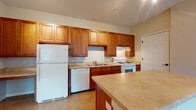Located at 5591 Rustling Way in Galloway, Ohio, this single-floor residence offers a functional and comfortable layout designed for everyday living. The kitchen is a standout feature, showcasing warm honey-toned wood cabinetry extending to the ceiling for generous storage, light-toned countertops, and a full suite of white appliances including a gas range, dishwasher, and refrigerator. A central island provides additional prep space and casual seating, while tile flooring adds durability underfoot. The open layout allows the kitchen to connect seamlessly to the living area, which is finished with plush carpeting and features a ceiling fan with a light fixture. Large sliding glass doors allow natural light to fill the space and provide access to the exterior. A dedicated bedroom offers carpeted flooring and a window with an outdoor view, creating a bright and relaxed atmosphere. The full bathroom is well-appointed with a rich wood vanity, a framed mirror, tile flooring, and a tub-shower combination. Track lighting and thoughtful details throughout contribute to the home's clean, cohesive aesthetic. The overall layout is efficient, making practical use of every area within the single-floor footprint.