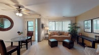 This single-floor residence is thoughtfully laid out to maximize functionality and comfort across its living spaces. The open-concept living and dining area serves as the heart of the home, featuring plush wall-to-wall carpeting, a ceiling fan, and a large picture window fitted with vertical blinds that allow abundant natural light to filter in. A sliding glass door connects the living area to an outdoor space, offering pleasant views of surrounding greenery. The dining area accommodates a round glass-top table and sits adjacent to the living room, creating a seamless flow between spaces.

The kitchen is outfitted with white cabinetry, ample counter space, and a stainless steel sink, providing a clean and practical workspace. Two well-proportioned bedrooms each feature large windows with vertical blinds, soft carpeting, and sliding-door closets offering generous storage. The primary bedroom is notably spacious, comfortably fitting a queen-sized bed alongside additional furnishings.

The full bathroom includes a white vanity with under-sink storage, a wall-mounted mirror cabinet, overhead lighting, and a full bathtub with a shower, finished with classic tile surround. Throughout the unit, neutral tones and consistent flooring create a cohesive and welcoming ambiance.