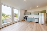 Located at 401 Union Ave SE in Olympia, WA, this 2-bedroom, 1-bathroom unit offers a thoughtfully designed single-floor layout with a clean, modern aesthetic throughout. The open-concept living and kitchen area serves as the heart of the unit, featuring light hardwood-style flooring that extends seamlessly through the space. The kitchen is outfitted with sage-toned cabinetry, stainless steel appliances including an electric range, dishwasher, and refrigerator, complemented by a wall-mounted range hood and ample upper and lower cabinet storage. Large, angled windows in the living area flood the space with natural light and offer views of the surrounding Olympia cityscape and greenery. A hallway connects the living area to the two bedrooms, each offering a calm, neutral palette with light flooring and closet storage — including sliding-door closets in the bedrooms. The combined bathroom and laundry room is clean and functional, featuring a full tub-shower surround, toilet, and hardwood-style flooring. Three closets throughout the unit provide generous storage options. Recessed lighting is present throughout, contributing to a bright, well-lit ambiance across all rooms.