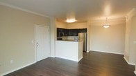 This single-floor residence showcases an open-concept design that seamlessly connects the kitchen and living areas, creating a cohesive and functional living environment. The kitchen is outfitted with dark espresso-toned cabinetry that provides a striking contrast against the warm beige walls. Stainless steel appliances, including a refrigerator and microwave, add a modern, polished touch. A white peninsula serves as both a workspace and a natural divider between the kitchen and the adjoining living area, offering casual seating potential while maintaining the open feel of the space.

The flooring throughout is a rich, dark hardwood-style material that lends warmth and visual continuity across the main living areas. The neutral beige walls and white trim create a clean, versatile backdrop well-suited to a variety of décor styles. Flush-mount ceiling lighting in the kitchen provides practical illumination, while a pendant light fixture is visible in the dining or living area, adding a decorative accent. The entryway features a classic six-panel white door with standard hardware, offering a tidy, welcoming entrance into the space. Overall, the layout feels open, practical, and move-in ready.