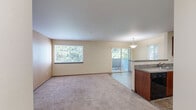 This one-bedroom, one-bathroom unit at Briarstone in Tacoma, Washington offers a thoughtfully designed, open-concept floor plan that makes efficient use of its space. The living room is bright and welcoming, featuring large windows that frame lush, green tree views and fill the room with natural light. Plush wall-to-wall carpeting adds warmth underfoot, while a sliding glass door leads directly to a private balcony, extending the living area outdoors. The kitchen is positioned adjacent to the living area, separated by a peninsula counter with a durable laminate countertop — ideal for casual dining or food prep. Rich warm-toned cabinetry, tile flooring, a double sink, and black appliances including a range and dishwasher complete the functional kitchen space. A pendant light fixture over the peninsula adds a finishing touch. The bedroom is a comfortable, carpeted retreat with ample wall space and access to a dedicated closet for storage. The full bathroom features a combined tub and shower unit, tile flooring, and a vanity with countertop storage. Neutral, warm tones are carried throughout the unit, creating a cohesive and inviting ambiance from room to room.