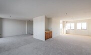 This two-floor residence offers a bright, open layout defined by neutral tones, plush carpeting throughout the living areas, and an abundance of natural light. The expansive main living area is a standout feature, with large sliding glass doors leading to a private balcony that frames open urban views. An additional wet bar with warm wood cabinetry and a sink provides a convenient serving area within the living space. The kitchen is well-appointed with white cabinetry, a coil-top range, refrigerator, dishwasher, and a stainless steel sink beneath a window, finished with easy-care tile flooring. The generous bedroom includes a built-in closet, an ensuite bathroom, and direct access to an additional room, offering flexible use of space. Two bathrooms are present in the unit, each featuring decorative floral wallcoverings that add a classic character. A secondary living or bedroom area is carpeted and filled with natural light from a pair of large windows overlooking the surrounding cityscape. Textured ceilings are consistent throughout, and the overall palette of cream and white tones creates a clean, neutral canvas throughout the entire residence.