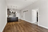 This one-bedroom, one-bathroom unit is designed to maximize functionality within a compact, single-floor layout. The open-concept kitchen and living area serves as the heart of the unit, featuring warm wood-look flooring, high ceilings, and a ceiling fan that enhances the sense of vertical space. A sliding barn door adds a distinctive architectural touch near the entryway.

The kitchen is outfitted with dark espresso cabinetry, granite-style countertops, and a peninsula with pendant lighting overhead — providing additional prep space and a casual dining option. Black appliances, including a refrigerator, range, and microwave, complete the kitchen suite.

The living area benefits from a large sliding glass door with vertical blinds, allowing natural light to fill the space. The bedroom is carpeted and includes a window with an outdoor view, and direct access to both the bathroom and a walk-in closet equipped with wire shelving for organized storage.

The bathroom continues the dark cabinetry theme with a granite-topped vanity, a large mirror, and wood-look flooring. Neutral wall tones throughout the unit create a clean, cohesive aesthetic well-suited for a variety of furnishing styles.