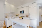 Located in the vibrant Kalorama neighborhood of Washington, DC, this one-bedroom, one-bathroom unit offers a thoughtfully designed layout with a clean, modern aesthetic. Light hardwood floors and crisp white walls run throughout, creating a bright and cohesive atmosphere from room to room.

The entry hallway welcomes you with recessed lighting and curated wall art, leading seamlessly into the open living area. The living room is bathed in natural light from large windows with neighborhood views, offering a comfortable and stylish retreat.

The combined kitchen and dining area is a standout feature, showcasing floor-to-ceiling flat-front white cabinetry, a marble-look tile backsplash, stainless steel appliances, and sleek white countertops. A central island provides additional prep and dining space, enhancing the kitchen's functional appeal.

The bedroom is a serene, well-proportioned space featuring large windows that invite abundant natural light and views of the surrounding neighborhood. A built-in closet and light flooring contribute to the room's calm, uncluttered feel.

The bathroom is finished with warm wood-toned wall tiles, a glass sliding shower enclosure with a rainfall showerhead, a wood-accented vanity, and polished concrete-style flooring, offering a spa-like sense of calm. A dedicated closet and hallway complete this well-appointed unit.
