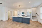 Located at 277 Clifton St SE in Atlanta, GA, this modern three-story home offers four bedrooms and four bathrooms thoughtfully distributed across its floors. The main level sets a striking tone with an open-concept layout featuring light hardwood flooring that flows seamlessly from the kitchen into the living area. The chef's kitchen is a standout, showcasing a large two-tone island with a crisp white quartz countertop and slate-blue cabinetry, complemented by white upper cabinets, stainless steel appliances including a French door refrigerator and electric range, and a modern pendant light fixture overhead. The adjoining living area benefits from abundant natural light through multiple windows and is outfitted with a ceiling fan. A staircase connects each level, with clean, contemporary railings tying into the home's modern aesthetic. The bedrooms are bright and airy, each featuring hardwood-style flooring, windows with outdoor views, and ceiling fans. Closets provide ample storage, with some rooms featuring sliding barn-style doors. The bathrooms maintain the home's modern design language, with dark-cabinetry vanities, white quartz countertops, undermount sinks, and matte black fixtures and hardware. The uppermost floor offers a more intimate retreat, ideal for a primary suite. Throughout, the home's clean white walls, recessed lighting, and consistent flooring create a cohesive, contemporary living environment.