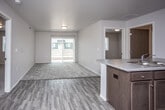 This single-floor unit offers a thoughtfully designed layout that balances open communal spaces with private living areas. The open-concept kitchen and living room form the heart of the unit, where durable wood-look flooring flows seamlessly underfoot. The kitchen is well-equipped with dark espresso cabinetry, light stone-style countertops, a double sink, and a full suite of black appliances including a refrigerator, electric range, and over-the-range microwave. A kitchen island with bar-style paneling provides additional workspace and a natural divide from the living area. The living room extends to a sliding glass door that fills the space with natural light and provides access to an outdoor area. Multiple bedrooms are finished with plush carpeting and feature windows that allow for ample natural light, offering comfortable and versatile spaces for rest or work. Two bathrooms serve the unit, each featuring wood-look tile flooring, dark vanity cabinetry, and a tub-shower combination. Clean white walls and neutral tones are carried throughout, creating a cohesive and move-in-ready environment. A utility room housing mechanical systems is also accessible from the kitchen area.