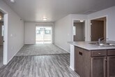 This single-floor unit offers a thoughtfully designed layout that balances open communal spaces with private living areas. The open-concept kitchen and living room form the heart of the unit, where durable wood-look flooring flows seamlessly underfoot. The kitchen is well-equipped with dark espresso cabinetry, light stone-style countertops, a double sink, and a full suite of black appliances including a refrigerator, electric range, and over-the-range microwave. A kitchen island with bar-style paneling provides additional workspace and a natural divide from the living area. The living room extends to a sliding glass door that fills the space with natural light and provides access to an outdoor area. Multiple bedrooms are finished with plush carpeting and feature windows that allow for ample natural light, offering comfortable and versatile spaces for rest or work. Two bathrooms serve the unit, each featuring wood-look tile flooring, dark vanity cabinetry, and a tub-shower combination. Clean white walls and neutral tones are carried throughout, creating a cohesive and move-in-ready environment. A utility room housing mechanical systems is also accessible from the kitchen area.