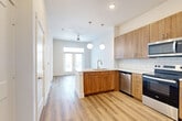 This thoughtfully designed one-bedroom, one-bathroom apartment in Austin, TX offers a clean, modern aesthetic with warm, contemporary finishes throughout. Light wood-tone vinyl plank flooring runs continuously across the entire floor plan, creating a cohesive and inviting atmosphere.

The open-concept kitchen is a standout feature, anchored by a central peninsula with a white quartz countertop and an undermount sink. Warm wood cabinetry, a classic white subway tile backsplash, and a full suite of stainless steel appliances — including a refrigerator with ice maker, electric range, built-in microwave, and dishwasher — complete the space. Globe pendant lights hang above the peninsula, adding a modern touch. The kitchen flows naturally into the living area, which features a ceiling fan and French doors that invite natural light.

The bedroom is a comfortable, well-proportioned retreat with a large window fitted with blinds offering views of greenery outside. A dedicated walk-in closet provides generous storage with multiple hanging rods and shelving.

The bathroom continues the warm wood cabinetry theme with a single-sink vanity, quartz countertop, a large mirror, and tiled shower surround, maintaining the consistent modern style found throughout the home.