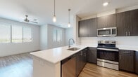 This well-appointed single-floor residence offers a thoughtfully designed layout with modern finishes throughout. The open-concept kitchen serves as the heart of the home, showcasing dark wood-grain cabinetry, crisp white quartz countertops, and a full suite of stainless steel appliances including a refrigerator, electric range, microwave, and dishwasher. A large peninsula with pendant lighting above provides both additional prep space and a natural gathering point that flows seamlessly into the living area. The living room is bright and airy, featuring light wood-style flooring, a ceiling fan, and multiple windows with horizontal blinds that invite natural light throughout the day. The bedrooms are finished with plush carpet flooring, ceiling fans, and windows offering outdoor views, creating comfortable and restful spaces. Each bathroom reflects the same contemporary design language found throughout the home, featuring dark wood-grain vanities, white quartz countertops, large framed mirrors with built-in shelving, and a tub-shower combination. The primary suite includes a walk-in closet with built-in shelving and hanging rods for generous storage. Clean white walls, consistent finishes, and a cohesive color palette give the entire residence a fresh, modern ambiance.