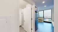 Located at 9 Homestead Place in Jersey City, NJ, this efficiently designed one-bedroom, one-bathroom residence offers a thoughtfully arranged single-floor layout with contemporary finishes throughout. Light wood-tone flooring flows seamlessly across the living areas, creating a clean and cohesive aesthetic.

The kitchen is compact yet well-appointed, featuring dark matte cabinetry — both upper and lower — paired with a white countertop, a stainless steel undermount sink, a smooth cooktop, a built-in stainless steel microwave, and a dishwasher. A white subway tile backsplash adds a modern touch to the space.

The bedroom is the most spacious room in the unit, highlighted by a large floor-to-ceiling window with black-framed sliding panels that flood the room with natural light and offer expansive views of the Jersey City skyline and surrounding urban landscape. A wall-mounted HVAC unit provides climate control. A fold-down wall-mounted desk or table is also present, maximizing utility within the room.

The bathroom is clean and minimal, finished with large-format neutral floor tiles, a dark-toned vanity with an integrated sink, and a separate walk-in shower stall with white subway tile walls and a glass enclosure. The overall design prioritizes functionality and modern simplicity throughout.
