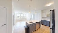 Located at 10 Patriot Pkwy in South Weymouth, MA, this well-appointed 2-bedroom, 2-bathroom residence offers a thoughtfully designed single-level layout with a clean, contemporary aesthetic throughout. The open-concept kitchen serves as the heart of the home, featuring a central island with a built-in sink, two-tone cabinetry with white upper cabinets and gray lower cabinets, a subway tile backsplash, stainless steel appliances including a refrigerator and range, and pendant lighting — all set atop light hardwood flooring that extends through the main living areas. Both bedrooms are carpeted for comfort, with the primary bedroom offering a generous footprint, and all bedrooms featuring large windows that invite natural light and frame peaceful green outdoor views. Each room includes dedicated closet space for ample storage. The two bathrooms are finished with neutral tile flooring, gray vanity cabinets, white quartz countertops, and subway-tiled tub-shower combinations, complemented by assist bars for added accessibility. The overall ambiance is bright, clean, and move-in ready, with a neutral color palette that lends versatility to any décor style.