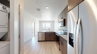 This well-appointed 1-bedroom, 1-bathroom unit offers a thoughtfully designed single-level layout with modern finishes throughout. The kitchen serves as a functional centerpiece, featuring rich dark wood cabinetry, granite countertops, a subway tile backsplash, and a full suite of stainless steel appliances including a French door refrigerator, electric range, over-the-range microwave, and dishwasher. A peninsula with an undermount sink and views toward a window brings natural light into the cooking area, enhancing the open feel of the living space. Light-toned hardwood-style flooring runs throughout the main living areas, complementing the crisp white walls and creating a bright, airy ambiance. The bedroom offers plush carpeting for comfort and includes access to a closet, providing practical storage. The bathroom is a standout feature, showcasing a dual-sink vanity topped with granite counters, dark wood cabinetry with brushed nickel hardware, a large wall mirror, and light wood-style flooring that ties seamlessly into the rest of the unit. The overall design balances contemporary aesthetics with everyday functionality, making this a practical and visually cohesive living space.