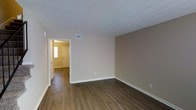 This two-story residence offers a well-organized layout with practical design choices throughout. The main level is characterized by rich, dark hardwood-style plank flooring that extends seamlessly across the living areas, complemented by warm beige and neutral-toned walls that create a welcoming ambiance. Natural light filters in through windows fitted with blinds, brightening the open living spaces. A closet near the entryway provides convenient built-in storage with a visible shelf and rod, adding functional value to the main floor. The staircase, positioned prominently in the main living area, features carpet treads and an elegant wrought iron railing, serving as a distinctive architectural accent while connecting the two floors. The textured ceilings add subtle visual depth to the rooms, while clean white baseboards and trim offer a crisp contrast to the warm wall tones. HVAC vents are integrated into the ceiling for efficient climate control. The open sightlines between rooms enhance the sense of space, with a clear view from the main living area through to the entryway. Overall, the space presents a clean, move-in-ready interior with a cohesive and practical design aesthetic.