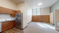 This 1-bedroom, 1-bathroom unit blends industrial character with modern finishes across a thoughtfully organized single-floor layout. The kitchen is a standout, featuring warm wood cabinetry extending to the ceiling, dark granite countertops, a classic white subway tile backsplash, and a full suite of stainless steel appliances including a French door refrigerator with water dispenser, electric range, over-the-range microwave, and dishwasher. Wood-style plank flooring runs through the kitchen and entry areas, adding warmth and durability.

The living area transitions seamlessly from the kitchen and is distinguished by exposed brick wainscoting along the walls, neutral carpet, and a grid-style window that allows natural light to pour in, creating a bright and inviting atmosphere. The high ceilings amplify the sense of openness throughout the space.

The bedroom continues the exposed brick aesthetic, offering a cozy yet spacious feel with carpet underfoot and access to a dedicated closet with built-in shelving. The bathroom is clean and functional, featuring wood-style flooring, a warm-toned wood vanity with a white countertop, a full-size soaking tub with shower, and crisp white walls. The entryway provides a practical welcome with wood-toned door and accessible electrical panel.