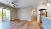 This thoughtfully designed 1-bedroom, 1-bathroom unit offers a practical and comfortable single-floor layout across six distinct spaces. The open living room features warm wood-look luxury vinyl flooring, neutral taupe walls, and a ceiling fan, creating a bright and airy atmosphere. Sliding glass doors lead to an outdoor balcony, filling the room with natural light and providing pleasant outdoor views.

The kitchen is well-equipped with crisp white cabinetry, light quartz countertops, a peninsula with a single-basin sink, and a full suite of stainless steel appliances including a gas range, over-the-range microwave, and refrigerator. The same wood-look flooring carries throughout the main living and kitchen areas, maintaining a cohesive aesthetic.

The bedroom offers plush wall-to-wall carpeting and a generously sized window that brings in natural light, accompanied by a dedicated closet for ample storage. The bathroom includes a full tub-shower combination with tile surround, a single-sink vanity with white cabinetry, light countertops, and a large mirror. A connecting hallway ties all rooms together efficiently, completing this clean, move-in-ready layout with consistent neutral tones and modern finishes throughout.