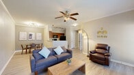 This 1-bedroom, 1-bathroom single-floor residence offers a thoughtfully designed open-concept layout that maximizes its comfortable footprint. Light wood-tone flooring flows throughout the main living areas, complemented by crisp white crown molding and neutral warm-gray walls that lend a clean, cohesive aesthetic.

The living room is bright and welcoming, featuring a ceiling fan with light fixture, large windows that allow natural light to fill the space, and a direct view into the adjoining dining and kitchen areas. The dining room sits adjacent to the kitchen peninsula, illuminated by a modern sputnik chandelier and track lighting, and is framed by the kitchen's half-wall pass-through — ideal for entertaining.

The kitchen is well-equipped with warm wood cabinetry, light countertops, a double-basin sink, and black appliances including a range, microwave, and refrigerator. The layout is efficient and highly functional.

The primary bedroom offers a comfortable, private retreat with a ceiling fan, a large window with outdoor views, and light wood flooring. Two closets provide ample storage throughout the unit. The bathroom includes a tub-shower combination, wood-toned cabinetry, a vanity with light countertop, and tile flooring. A dedicated laundry area and hallway complete this well-organized and practical home.