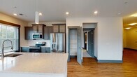 Located at 4964 NC-55 in Cary, North Carolina, this thoughtfully designed single-floor unit offers a contemporary living experience with high-quality finishes throughout. The open-concept kitchen is a standout feature, showcasing sleek quartz countertops, a large center island with an undermount sink, and a full suite of stainless steel appliances including a French door refrigerator, electric range, and built-in microwave. Dark gray cabinetry with glass-front upper panels and a classic subway tile backsplash complete the kitchen's modern aesthetic. Warm hardwood-style flooring flows seamlessly through the kitchen, living, and hallway areas, creating a cohesive and inviting atmosphere. The living area is bright and airy, benefiting from large windows with blinds that allow natural light to fill the space, complemented by a ceiling fan overhead. Bedrooms are carpeted for comfort and include ceiling fans, windows with outdoor views, and walk-in closets with built-in shelving. The bathrooms are elegantly appointed with gray vanity cabinetry, quartz countertops, and white subway tile tub surrounds. A dedicated in-unit laundry room with full-size washer and dryer adds everyday convenience. The overall design palette of cool grays, warm wood tones, and crisp white surfaces gives this unit a clean, modern character.