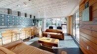 Located at 1600 15th Street in San Francisco's SoMa neighborhood, The Well is a thoughtfully designed single-floor commercial space that blends warm, natural materials with modern functionality. The interior is anchored by rich warm-toned wood wall paneling that runs throughout, complemented by dark hardwood flooring and ornate embossed tin ceilings that lend the space a distinctive character.

The lounge area is furnished with supple leather sofas and a sculptural wooden coffee table, creating an inviting gathering atmosphere bathed in natural light from expansive floor-to-ceiling sliding glass doors. These doors open directly onto an outdoor terrace, seamlessly extending the usable space and allowing for abundant natural light and outdoor views.

The bar area, branded "The Well – Stir It Up," features a wood-paneled counter with industrial-style metal barstools and a striking blue geometric tile backsplash that serves as a bold focal point. Adjacent to the bar, a fully equipped commercial kitchen offers stainless steel countertops, professional-grade appliances including a gas range with grill, commercial ventilation hoods, and subway tile walls — ideal for catering or event use.

Large potted plants, colorful artwork, and carefully curated décor add personality throughout. The space is well-suited for events, social gatherings, or community programming, offering a cohesive blend of comfort and functionality.
