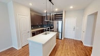 This single-floor residence showcases a thoughtfully designed open layout with consistent modern finishes throughout. The kitchen serves as a central highlight, featuring dark espresso-toned cabinetry with sleek hardware, a bold teal glass tile backsplash, and a full suite of stainless steel appliances including a French door refrigerator, electric range, and built-in microwave. A central island with a white quartz countertop and undermount sink provides additional prep space, while a trio of pendant lights hang above on a track rail. A dedicated built-in wine rack adds a distinctive touch near the entry door. Warm wood-look flooring extends through the kitchen and living areas, complemented by recessed lighting and a ceiling fan.

The living area offers direct outdoor access through a set of French doors that bring in natural light and exterior views. Bedroom spaces feature plush carpeting, ceiling fans, and windows with exterior views, providing a quiet and comfortable retreat. The bathroom is finished with large-format tile flooring, dark wood vanity cabinetry, granite countertops, a framed mirror, and a glass-enclosed shower, delivering a clean and contemporary aesthetic throughout.