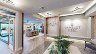The Camelot West at Townelake clubhouse in Sayreville, NJ, is a thoughtfully designed single-floor amenity space offering generous square footage across its interconnected areas. The entrance features a branded reception area with warm wood accents, pendant lighting, and stone-inlaid flooring details that establish a polished, modern aesthetic throughout.

The main lounge is an inviting gathering space anchored by a tiered crystal chandelier and a large wall-mounted display. Neutral-toned seating, light wood-plank flooring, and wood-wrapped structural columns contribute warmth and sophistication. Floor-to-ceiling glass doors open toward an outdoor area, filling the room with natural light and outdoor views.

Adjacent to the lounge, a wet bar area features marble countertops, dark wood cabinetry with brushed gold hardware, integrated appliances, and pendant lighting — ideal for entertaining. A billiards table rounds out the social zone.

The fitness center is generously proportioned, outfitted with cardio machines, strength equipment, free weights, and ceiling fans. Linear LED lighting, mirrored walls, and large windows overlooking greenery create an energizing environment. Together, these spaces deliver a cohesive, upscale community experience.